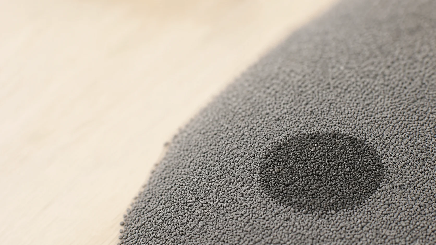 A patch of litter darkened where it has just absorbed moisture, with dry grains all around it.